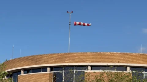 Red and White Windsock Blowing in Strong Wind Above Curved Wooden Stadium Roof Stock Footage 345518941
