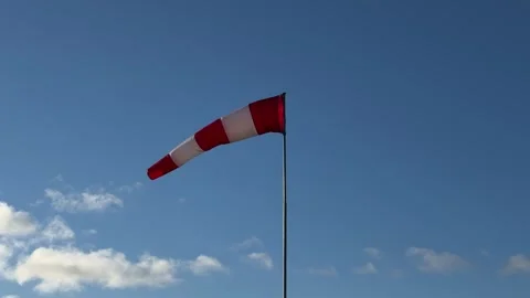 Red and white windsock on a pole against a clear blue sky with scattered clouds Stock Footage 294036932
