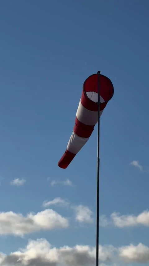 Red and white windsock on a pole against a clear blue sky with clouds. Verical Stock Footage 294036946