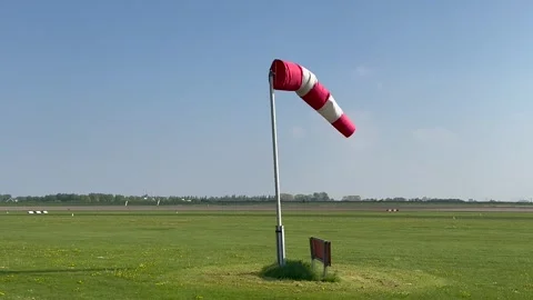 A red and white windsock stands beside a grassy airport Stock Footage 344987601