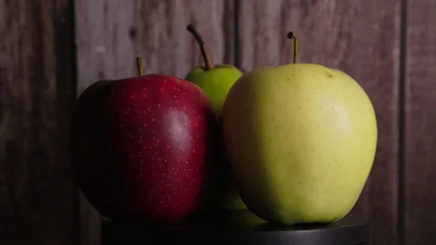 Red and yellow apples with a green pear rotate on a brown wooden background Stock Footage 330687205