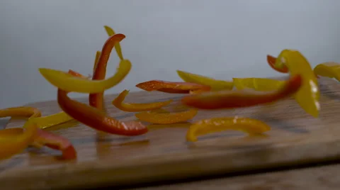 Red and yellow bell pepper slices falling in slow motion onto a cutting board Stock Footage 64585696
