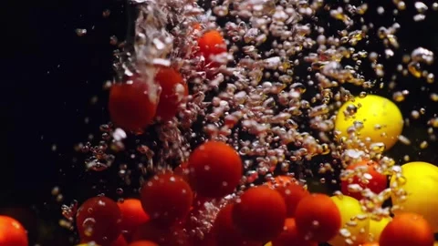 Red and yellow cherry tomatoes falling in transparent water on black background. Stock Footage 249229083