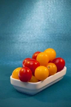 Red and yellow cherry tomatoes in a white plate on a blue background Stock Photos