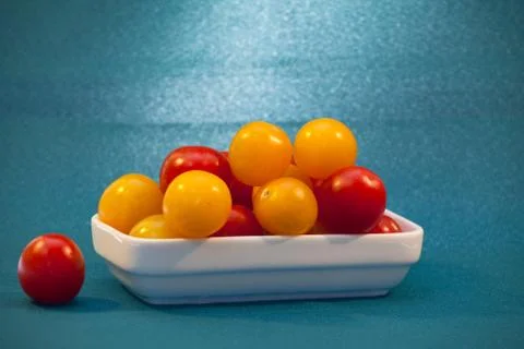 Red and yellow cherry tomatoes in a white plate on a blue background Stock Photos