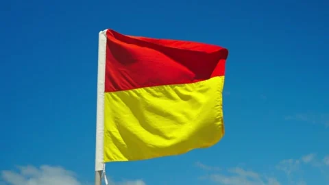 A red and yellow flag waves in the wind against a blue sky, marking designated Video stock 307277956