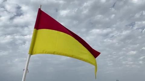 Red and yellow warning flag on the beach flutters in the wind Stock Footage 240489131