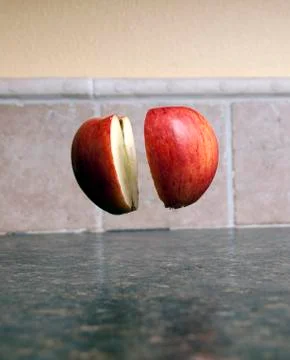Red apple being cut in half with a sharp knife being held up by one single to Stock Photos