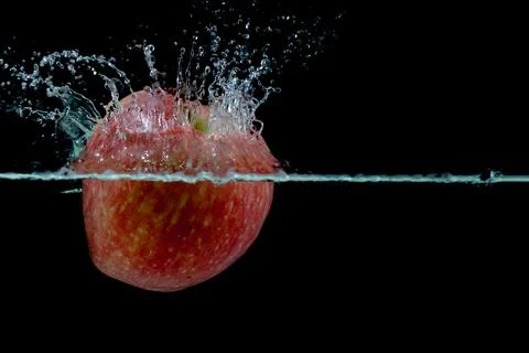 Red apple fall into water with splashes on black background, place under text Stock Photos