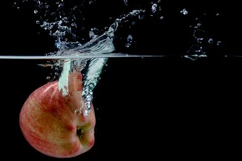 Red apple fall into water with splashes on black background, place under text Stock Photos