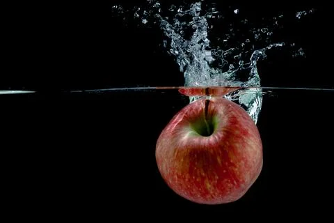 Red apple fall into water with splashes on black background, place under text Stock Photos