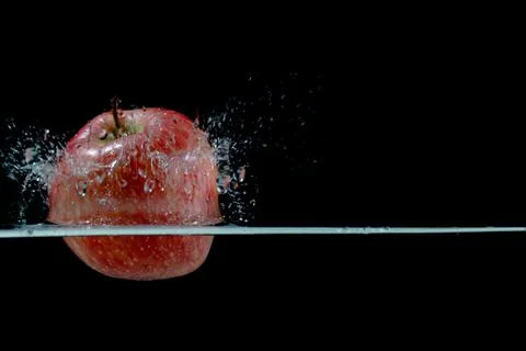 Red apple fall into water with splashes on black background, place under text Stock Photos
