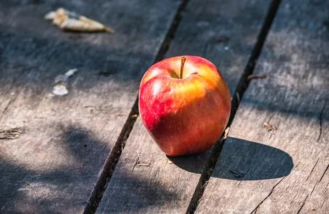 The red apple lit by the sun casts shadows on an old wooden planked surface. Stock Photos