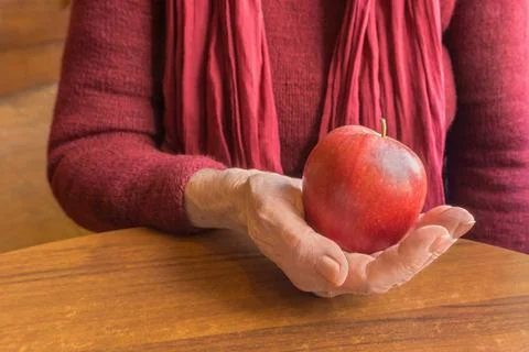 Red apple in old hands of elderly women in red, close up Foto stock