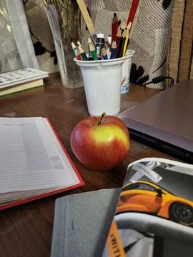 Red apple on open book under desk lamp Stock Photos