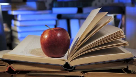 Red apple resting on open book with turned pages in library setting Stock Footage 336044352