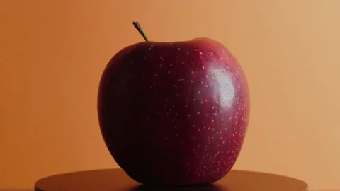 A red apple rotates around its axis on an orange background Stock Footage 330687250