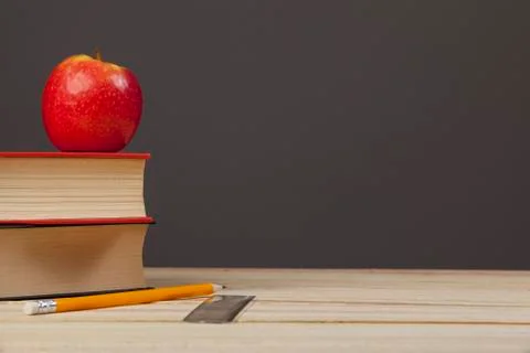 Red apple sitting on top of some books on desk top Stock Photos