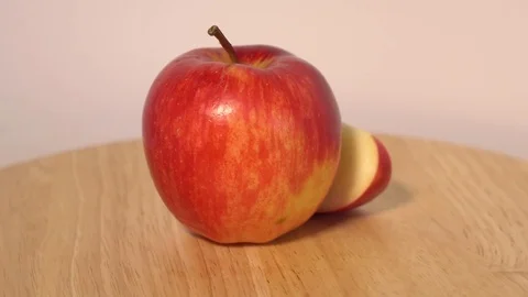 Red apple with slice rotating on wooden table Stock Footage 76543548
