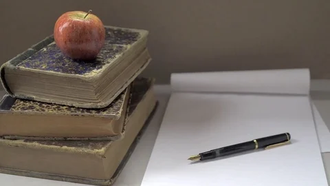 Red apple on three stacked books, a fountain pen and a notebook. Dolly shot Stock Footage 73867594