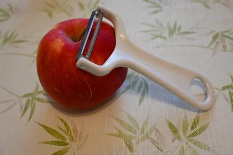 Red apple with vegetable peeler on patterned tablecloth Stock Photos