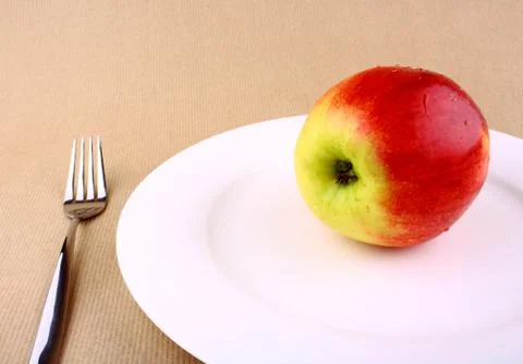 Red apple on white plate with fork Stock Photos