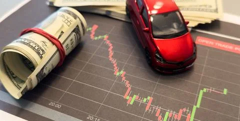 Red arrow graphics down on the background of the car and a stack of money c.. Stock Photos