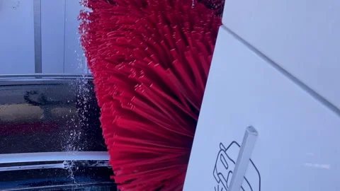 Red automatic car wash brushes spinning along a vehicle side, water and foam Vidéo 333036867