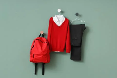 Red backpack and school uniform with sweater, shirt, and trousers hanging on  Stock Photos