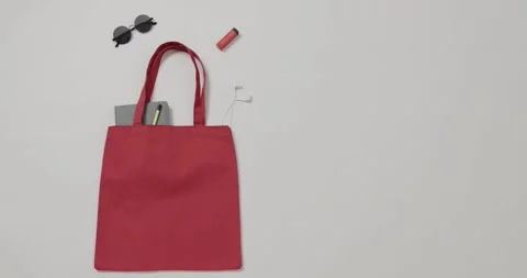 Red bag with sunglasses, notebook, lipstick, earphones on white background, copy Stock Footage 331246114