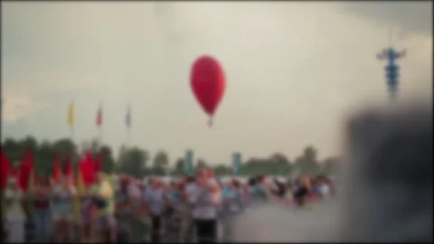Red Balloon Floats Over Crowd At Outdoor Festival. Blurred Scene Of People And Stock Footage 323908771