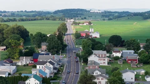 Red barn and grain silos rise beside curving country road through small farm Stock Footage 340969817
