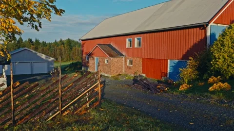 A Red Barn and White Garage Sit Beside a Rustic Fence, With Autumn Foliage Stock Footage 333148843