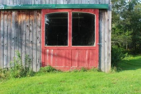 Red barn doors with large windows in green track on a weathered wood building Stock Photos
