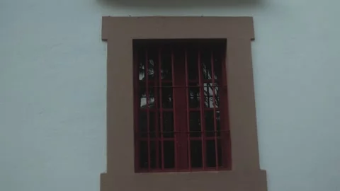 Red barred window with a white wall and brown frame, typical of traditional Stock Footage 305017740