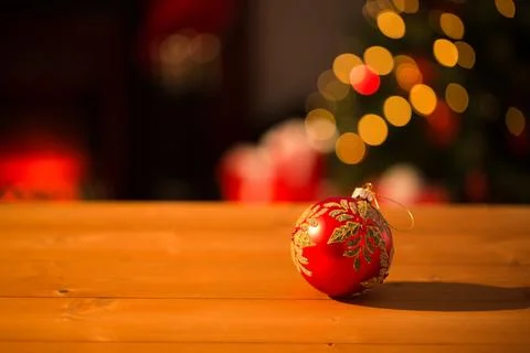 Red bauble with gold leaf is resting on wooden tabletop in 3D render, glowing Stock Illustration