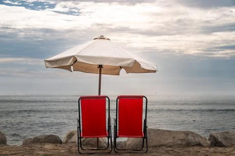 Red beach chairs under white umbrella facing Pacific Ocean at tranquil Huanchaco Stock Photos