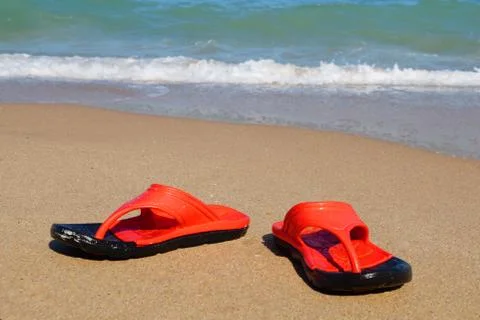 Red beach slates on an empty sandy beach near the sea waves. Stock Photos