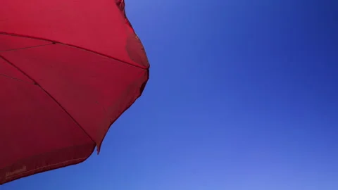 Red Beach Umbrella Fluttering in Wind Blue Sky Stock Footage 344947509