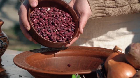 Red beans are poured from a clay brown pot onto a linen tablecloth Video stock 129530184