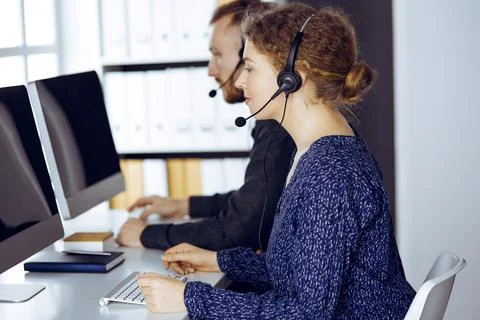 Red-bearded businessman talking by headset near his female colleague while Stock Photos