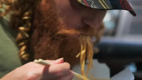 Red bearded guy eats Chinese udon with meat and vegetables in wok close up Stock Footage 279206362
