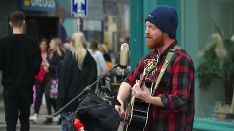 Red beared man playing and singing the guitar in the streets Stock Footage 220683239