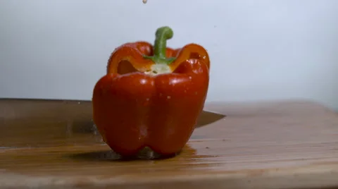 A red bell pepper being chopped in half on a cutting board in slow motion. Stock Footage 64580547
