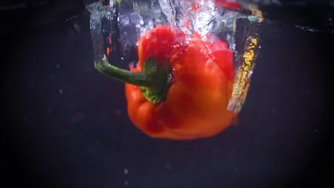 Red bell pepper falls into water. Slow motion. Black background. Food video Video stock 122979620