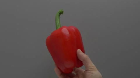 Red bell pepper in hand on a gray background. Видео 265867939
