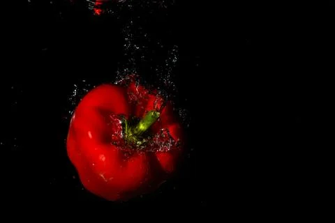 Red bell pepper in water with splash on black background. Stock Photos