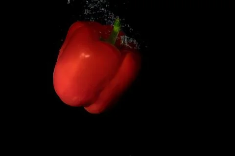 Red bell pepper in water with splash on black background. Stock Photos