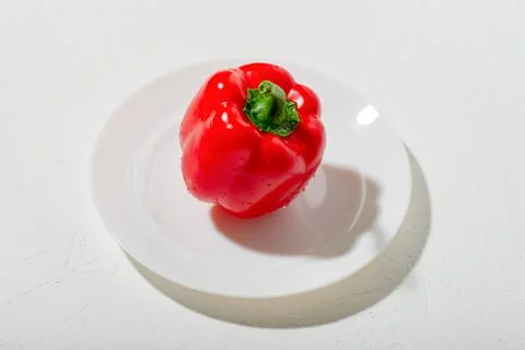 Red bell pepper on a white plate. White background. Fresh raw pepper. Stock Photos