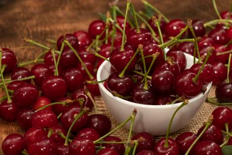 Red berries of a cherry in a white ceramic bowl. On a wooden background. A lo Foto stock